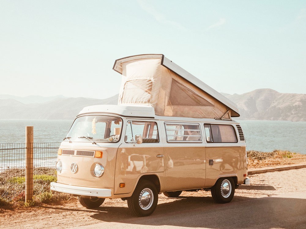 fotografía de una VAN beige aparcada y detrás la playa